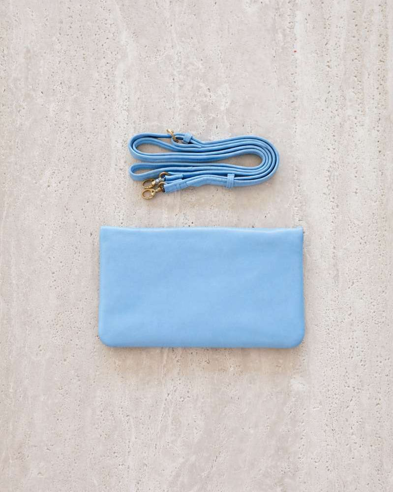 Light blue agatha phone wallet with matching strap on a textured beige surface