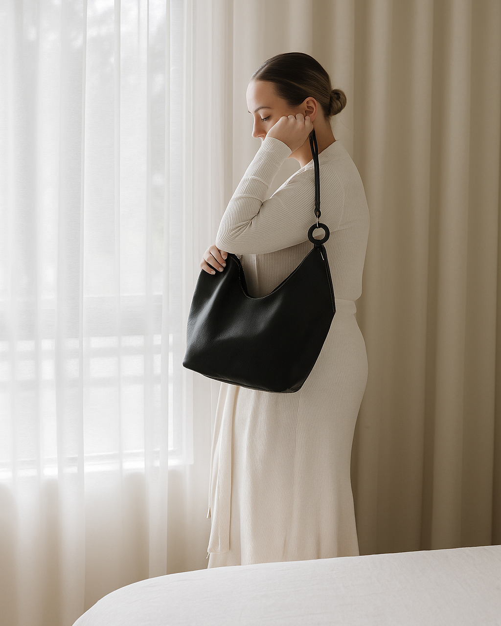 Woman holding a black ovae handbag in front of a window with white curtains