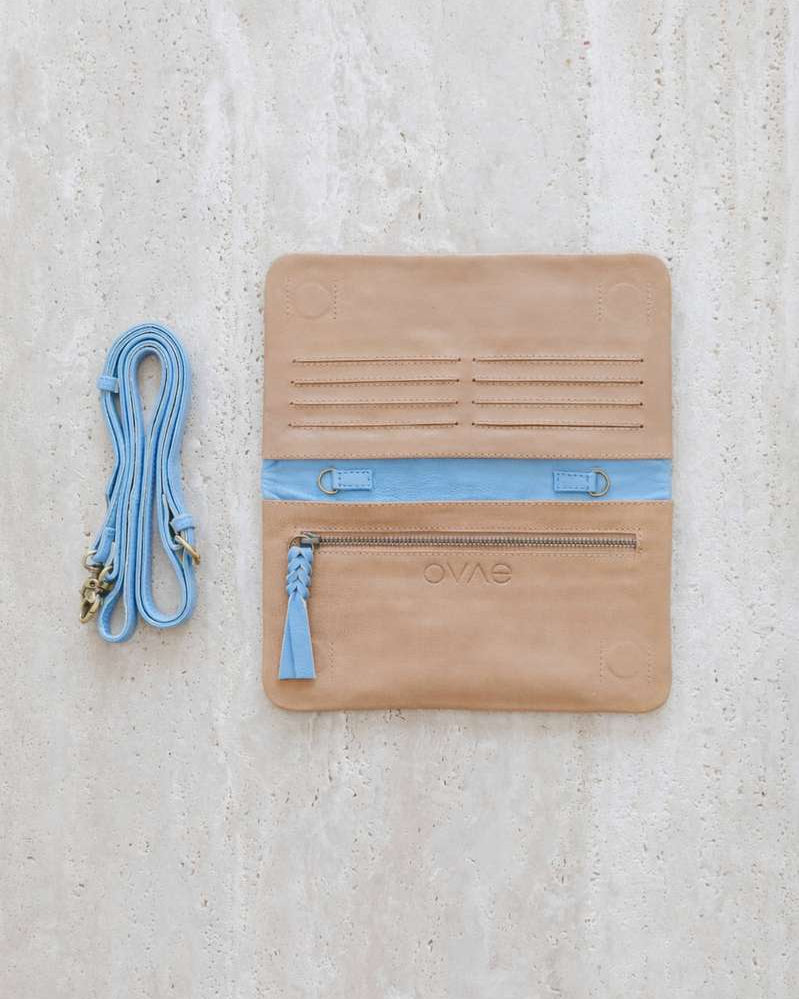 Tan leather pouch with blue accents and a matching strap on a light gray background