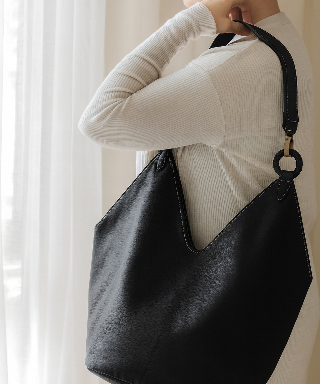 Person holding a black leather handbag against a neutral background brand ovae