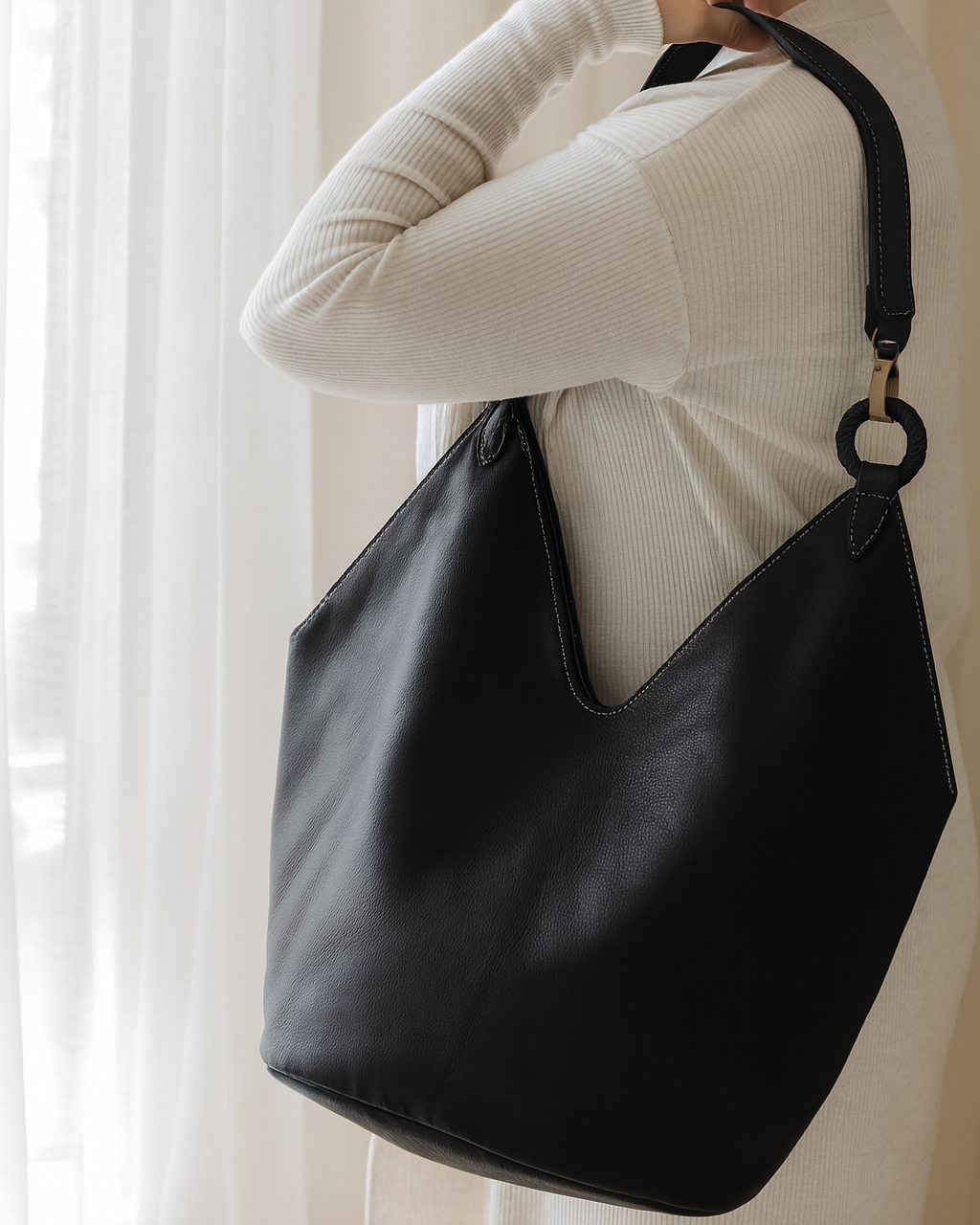 Person holding a black leather handbag against a neutral background brand ovae