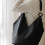 Person holding a black leather handbag against a neutral background brand ovae
