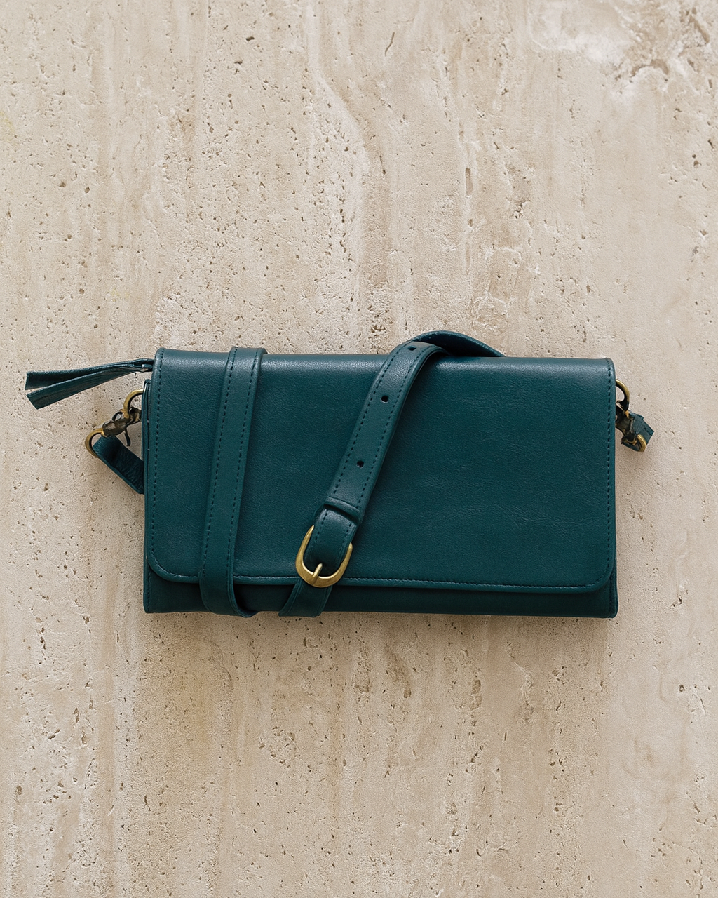 Teal leather handbag with a strap on a beige textured background