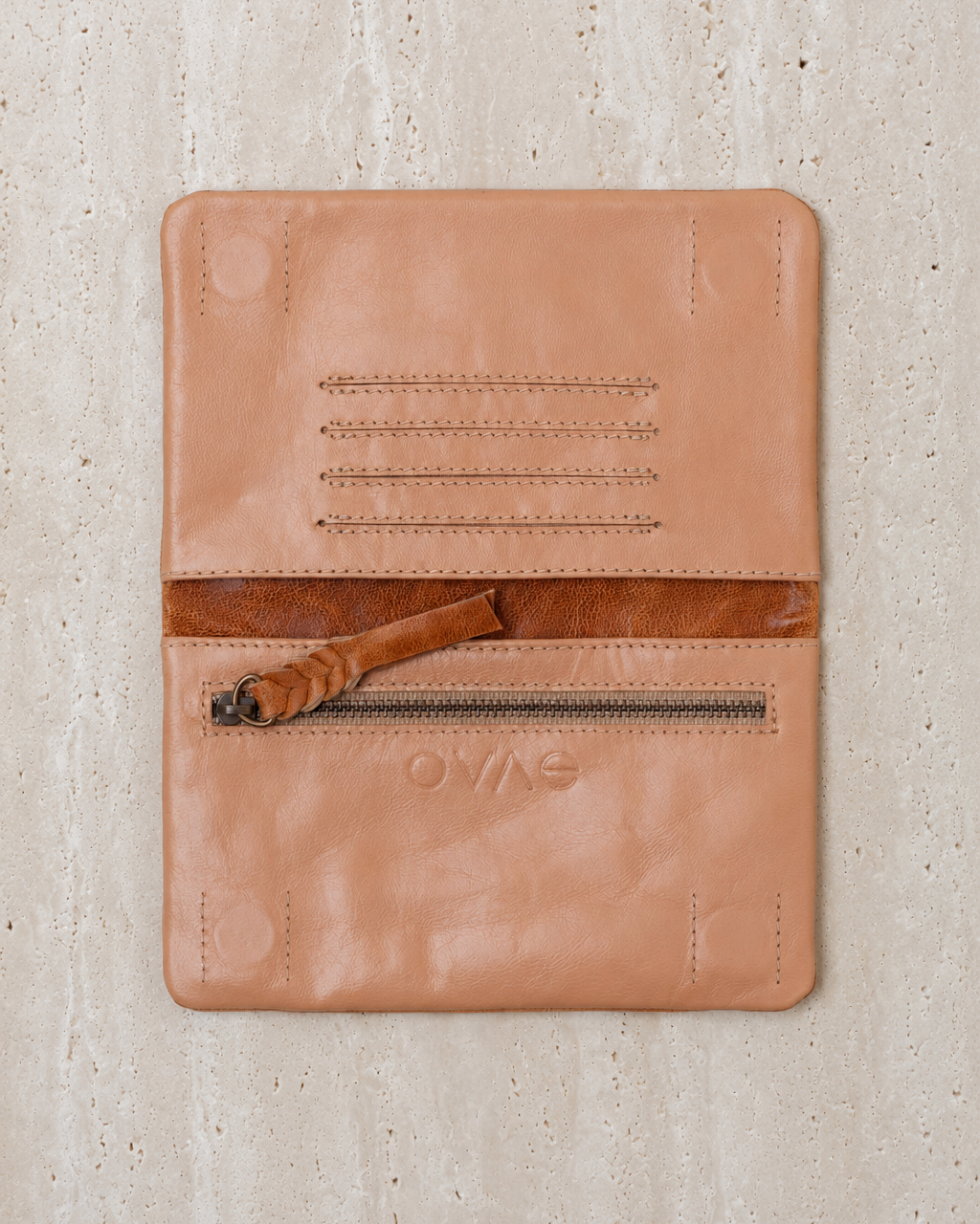 Ovae Tan leather wallet with zipper on a textured beige background