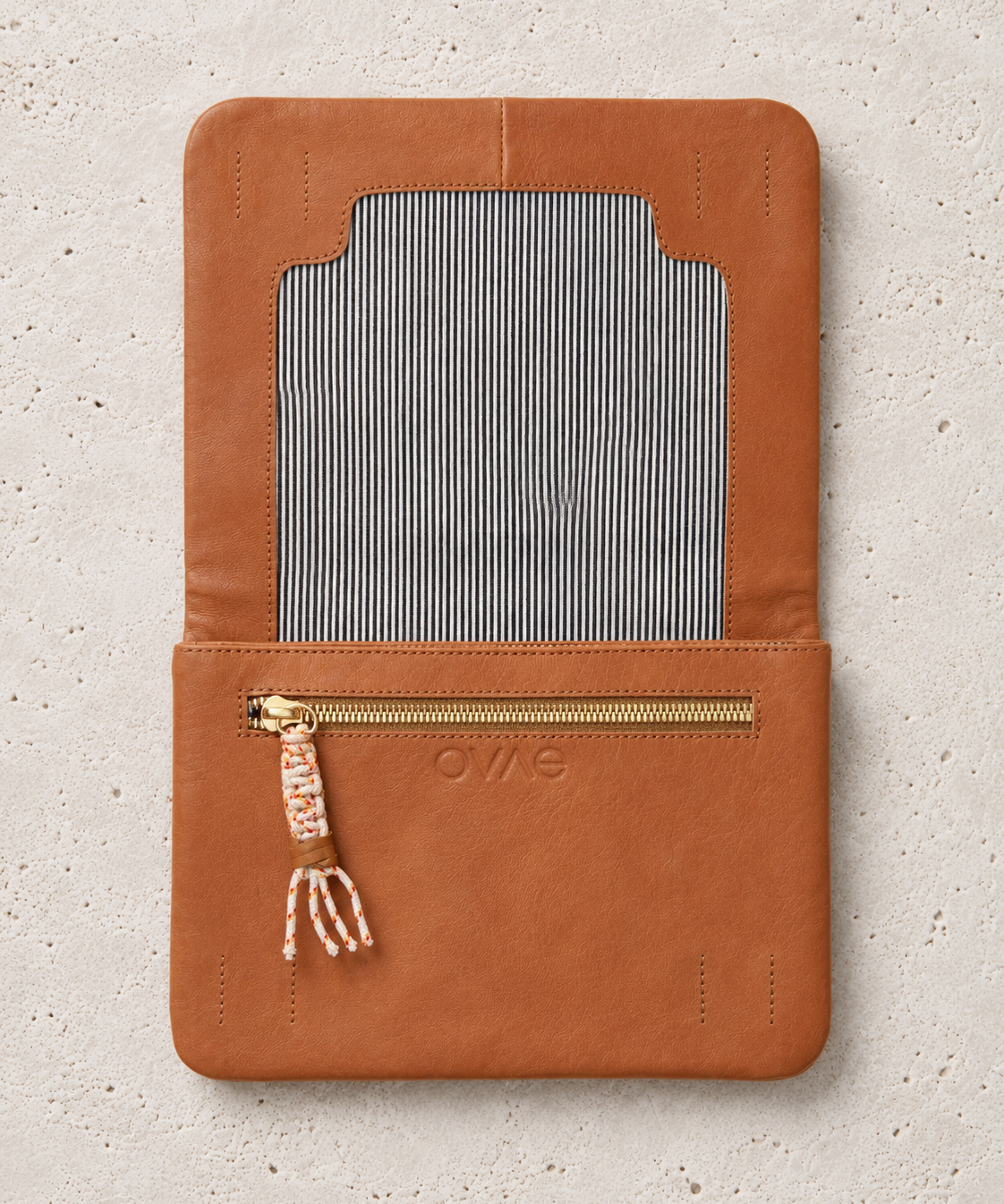 A tan leather wallet or organizer cover with a striped fabric insert and a gold zipper pocket, shown flat on a light textured background. The brand name 'OWS' is embossed on the front.