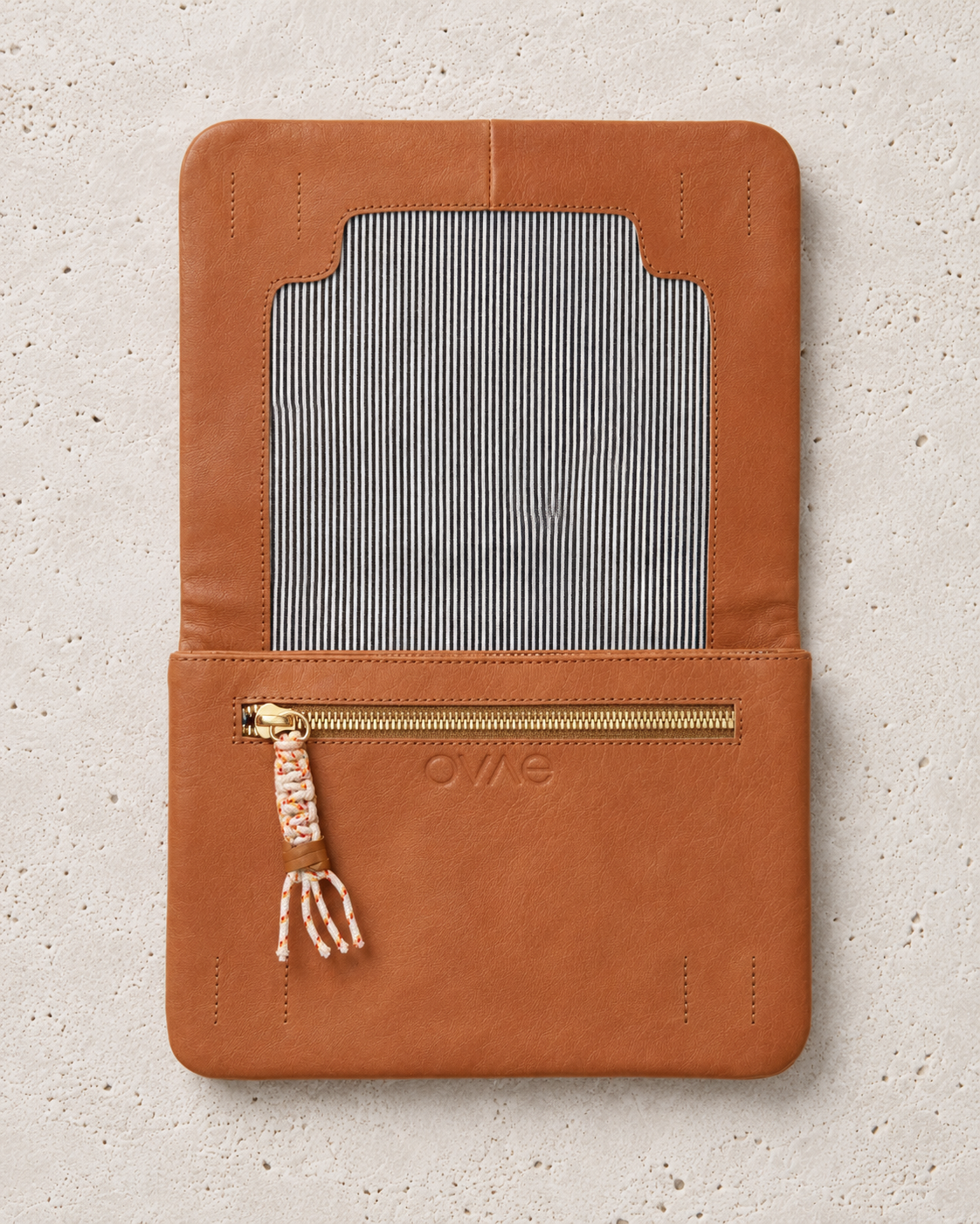 A tan leather wallet or organizer cover with a striped fabric insert and a gold zipper pocket, shown flat on a light textured background. The brand name 'OWS' is embossed on the front.