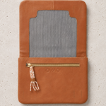 A tan leather wallet or organizer cover with a striped fabric insert and a gold zipper pocket, shown flat on a light textured background. The brand name 'OWS' is embossed on the front.