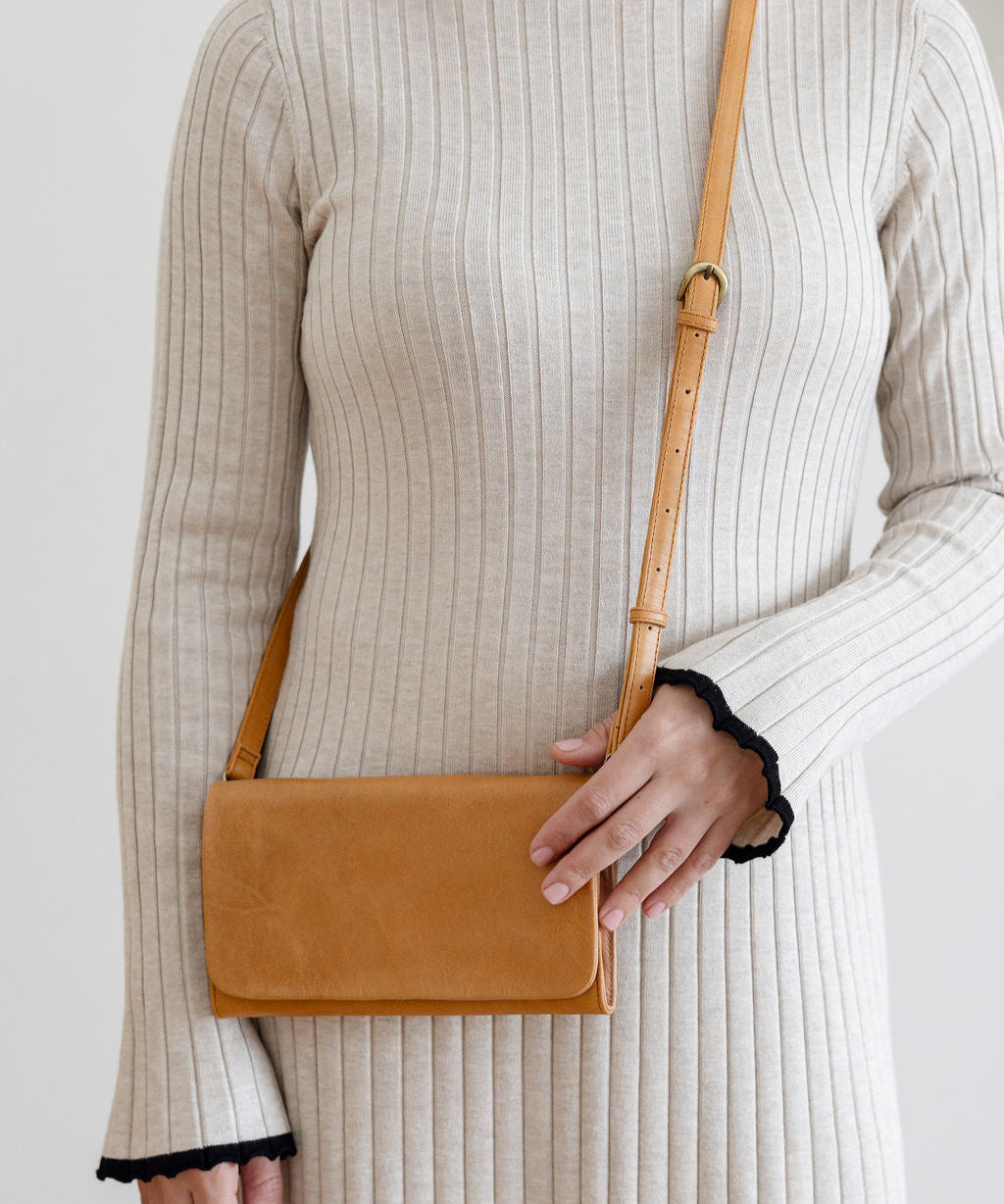 Person wearing a beige ribbed dress holding a brown leather bag against a plain background