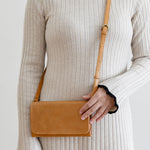 Person wearing a beige ribbed dress holding a brown leather bag against a plain background