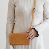 Person wearing a beige ribbed dress holding a brown leather bag against a plain background