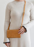 Person wearing a beige ribbed dress holding a brown leather bag against a plain background