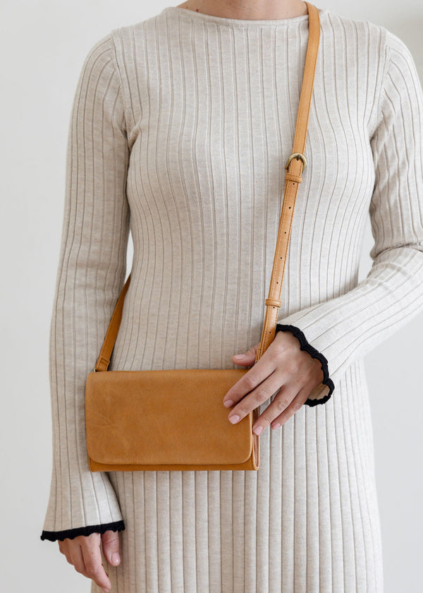 Person wearing a beige ribbed dress holding a brown leather bag against a plain background