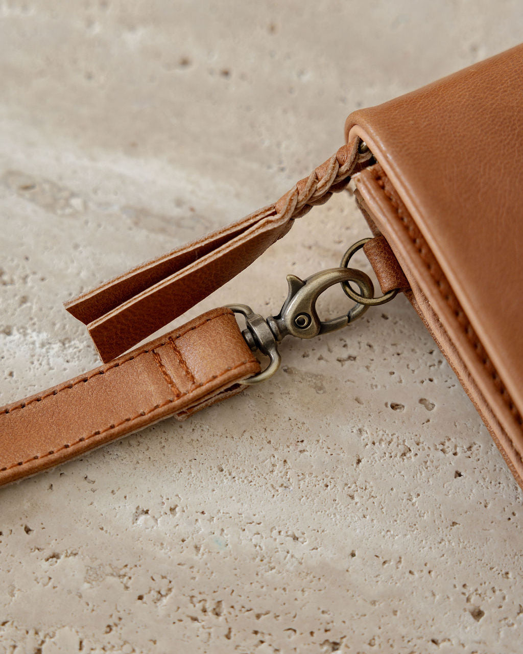 Brown leather wallet with strap on a textured beige surface