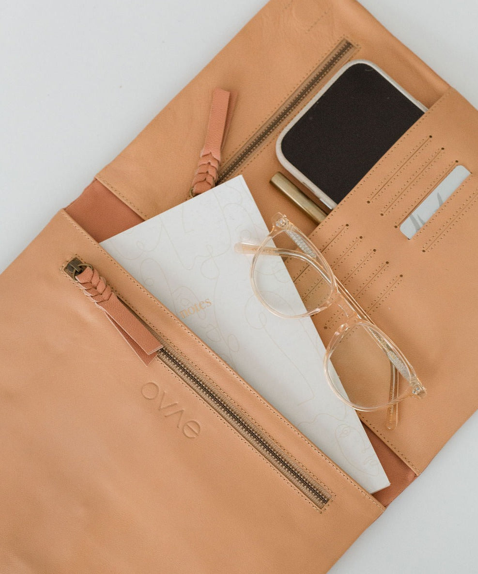 A beige leather organiser with multiple compartments, shown open with a tablet, iPhone, glasses, and other items arranged within.