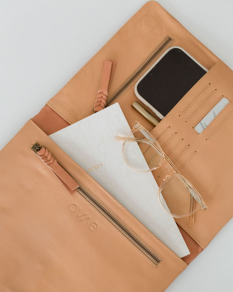 A beige leather organiser with multiple compartments, shown open with a tablet, iPhone, glasses, and other items arranged within.
