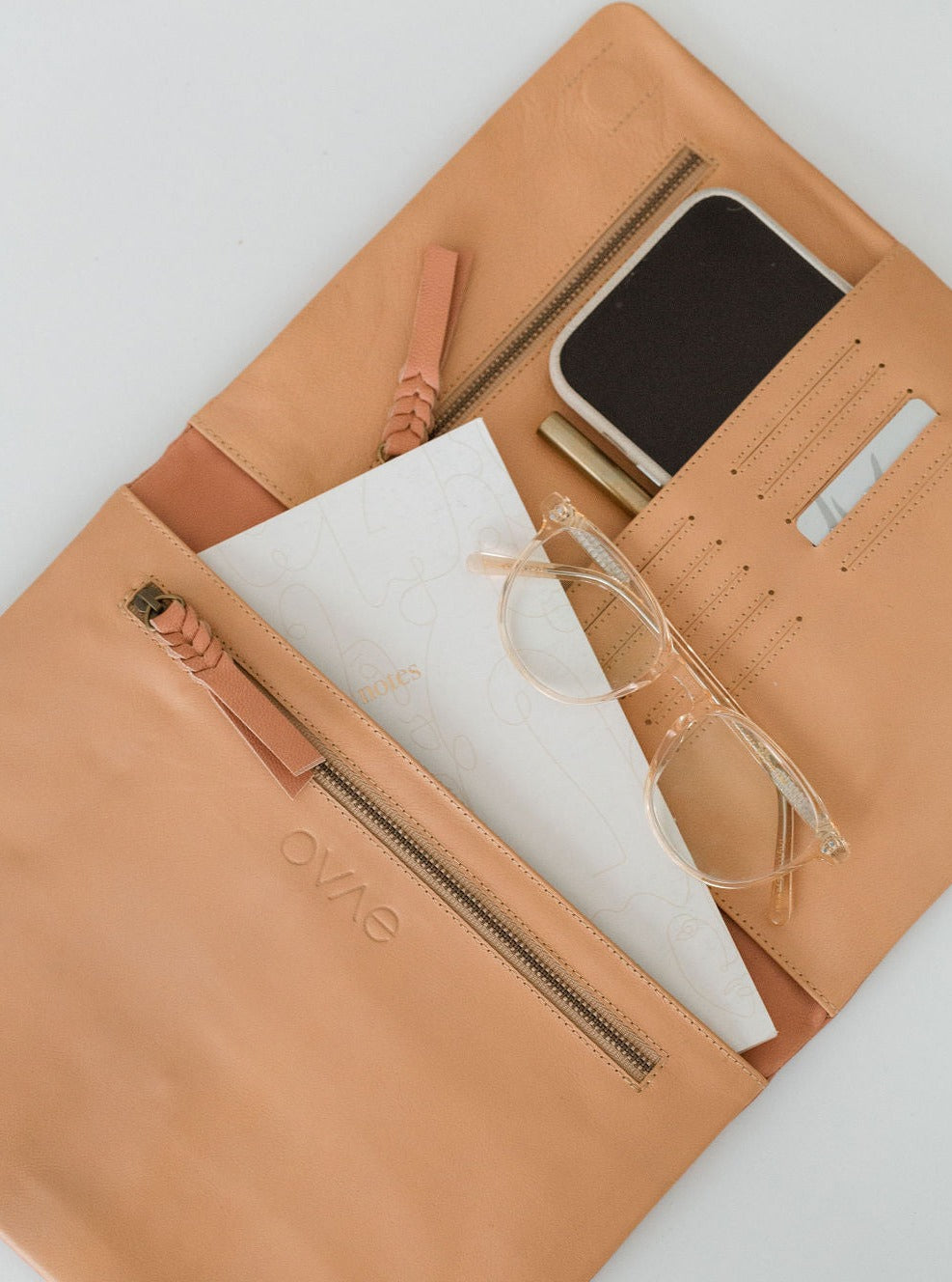 A beige leather organiser with multiple compartments, shown open with a tablet, iPhone, glasses, and other items arranged within.