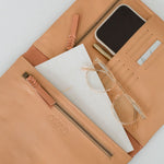 A beige leather organiser with multiple compartments, shown open with a tablet, iPhone, glasses, and other items arranged within.