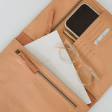 A beige leather organiser with multiple compartments, shown open with a tablet, iPhone, glasses, and other items arranged within.